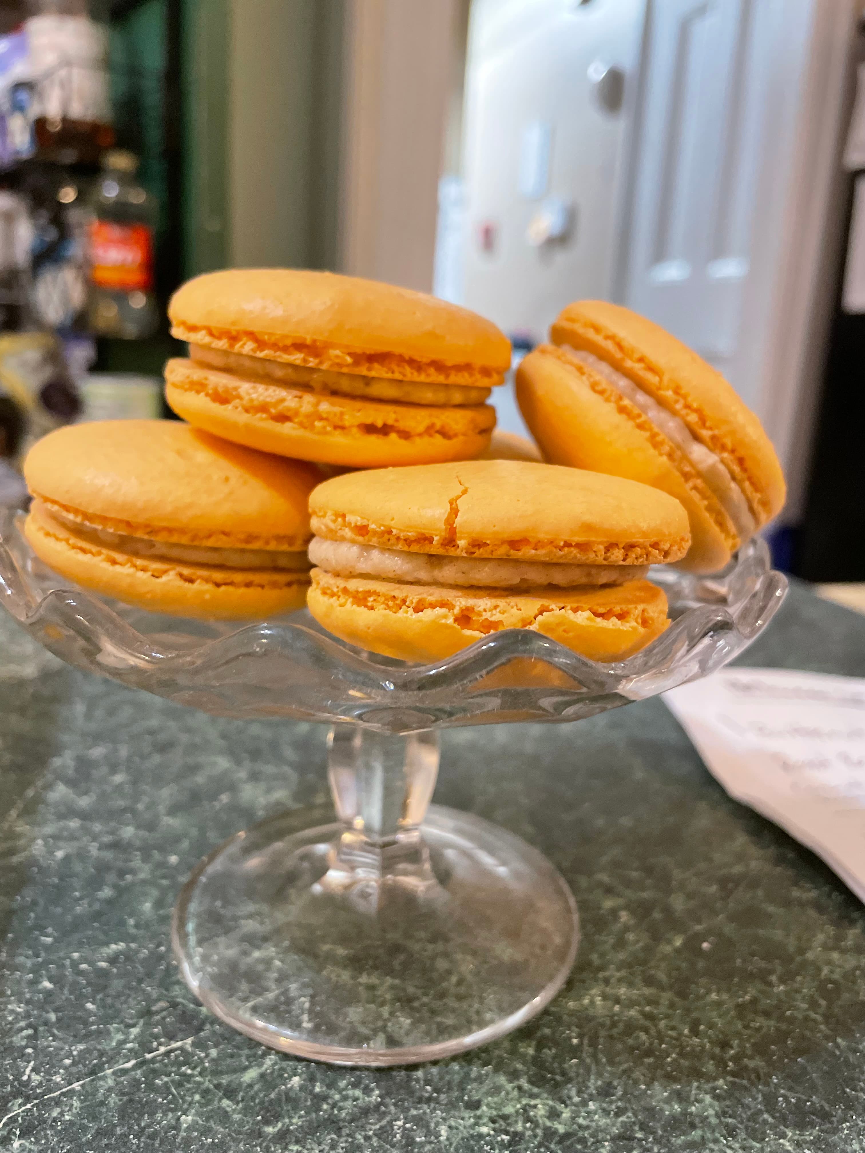 A glass dish holds several golden-yellow macarons.