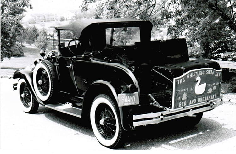 A vintage black and white photograph of a classic car with a sign advertising a bed and breakfast.
