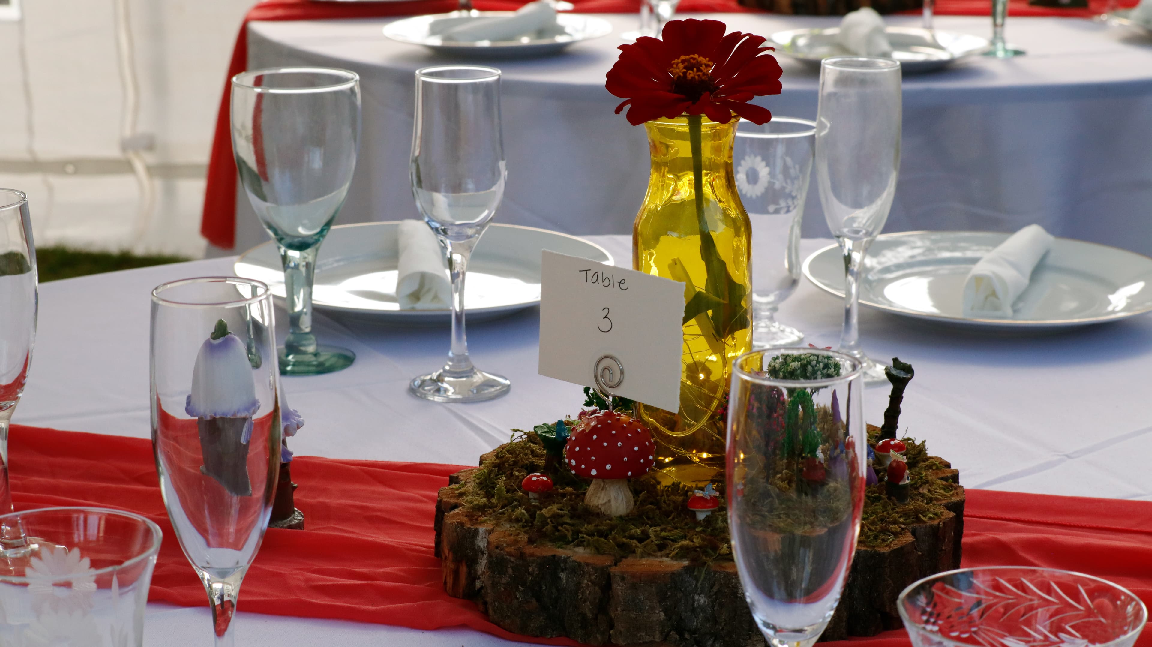 A table setting featuring a decorative yellow vase with a flower, a sign indicating "Table 3," and various glasses and plates.