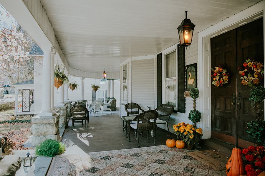 A welcoming porch adorned with autumn decorations, chairs, and pumpkins.