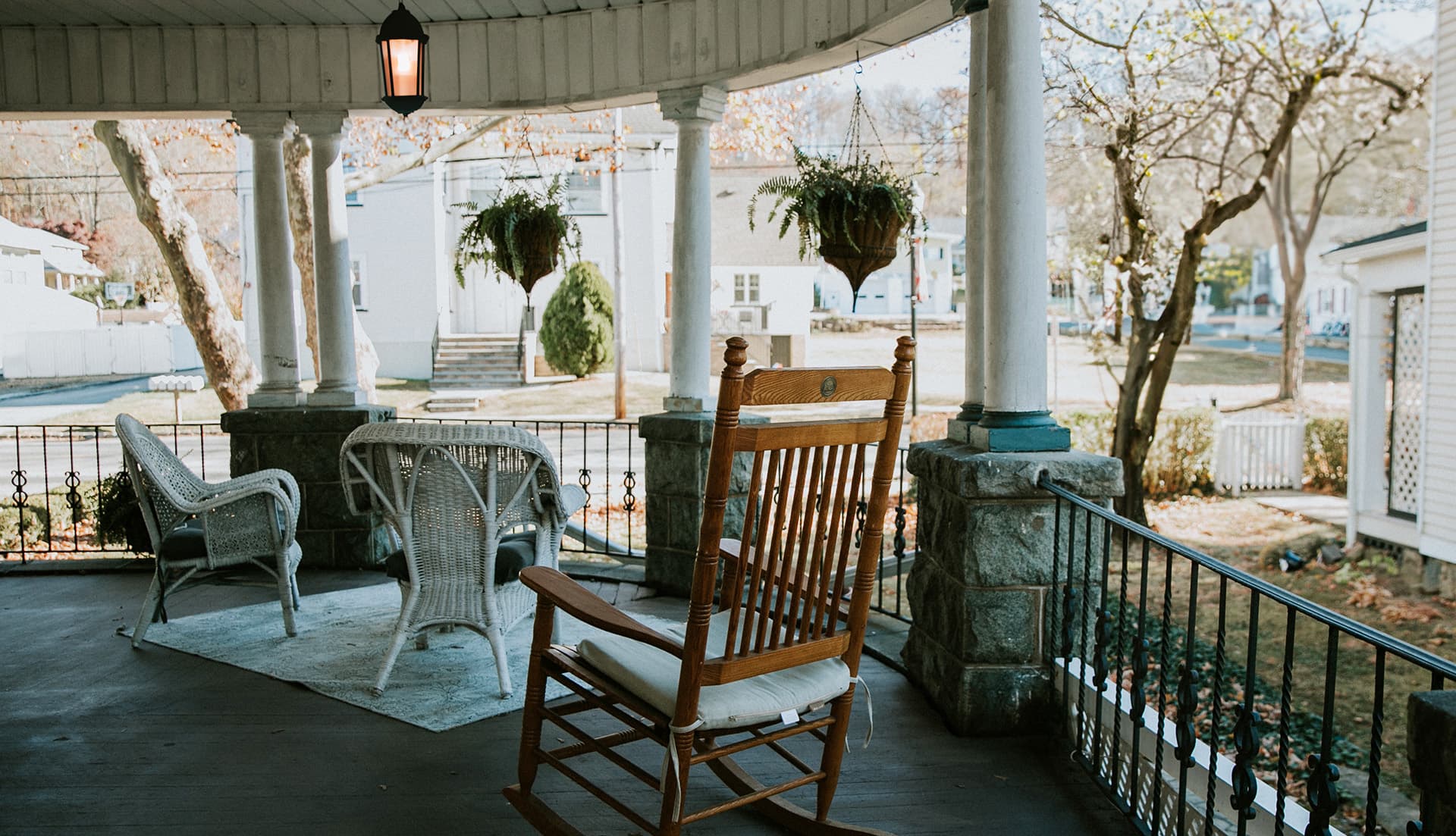 A cozy porch featuring a rocking chair, wicker furniture, and hanging plants.