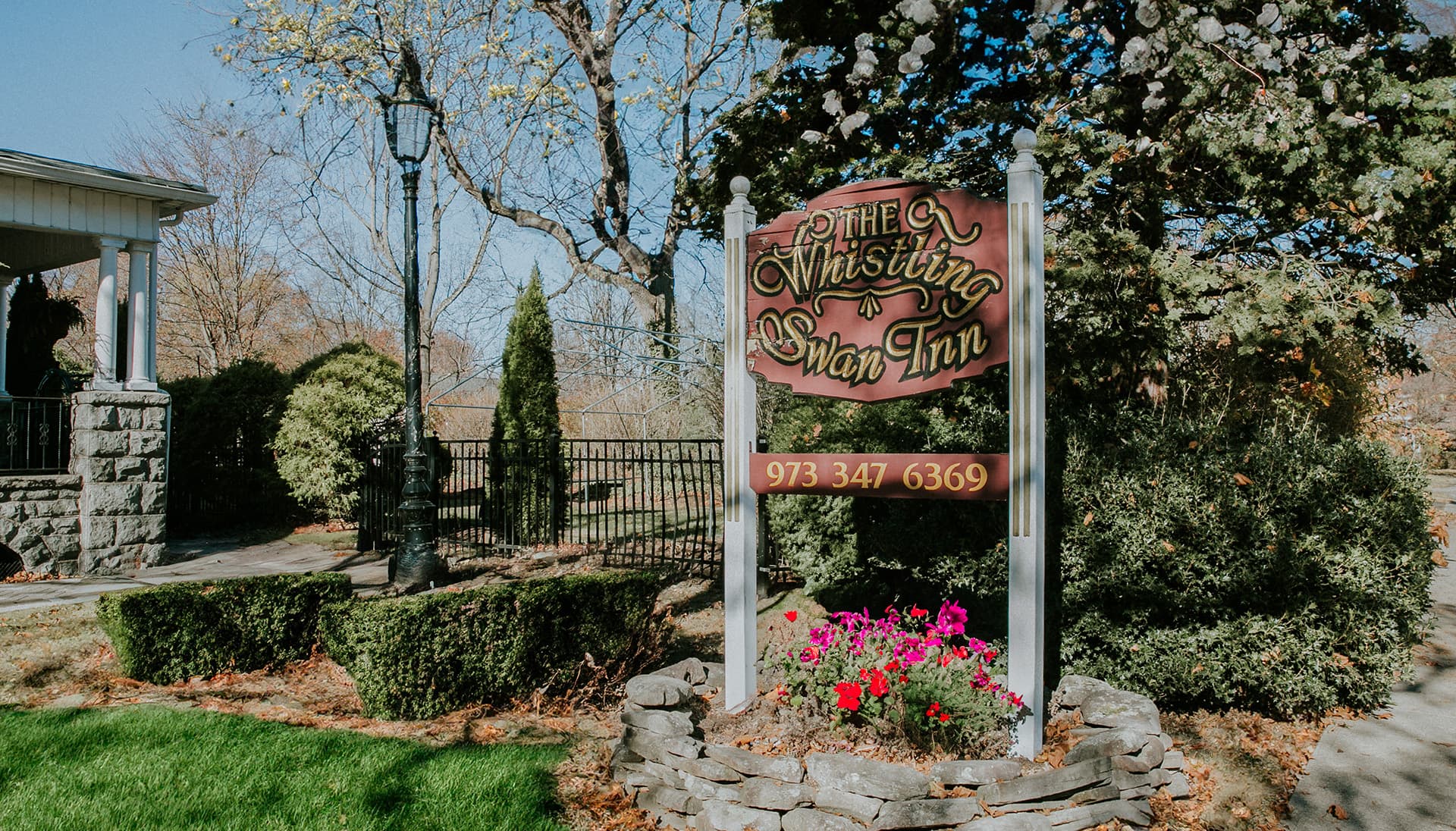 A welcoming sign for The Whistling Swan Inn surrounded by greenery and flowers.