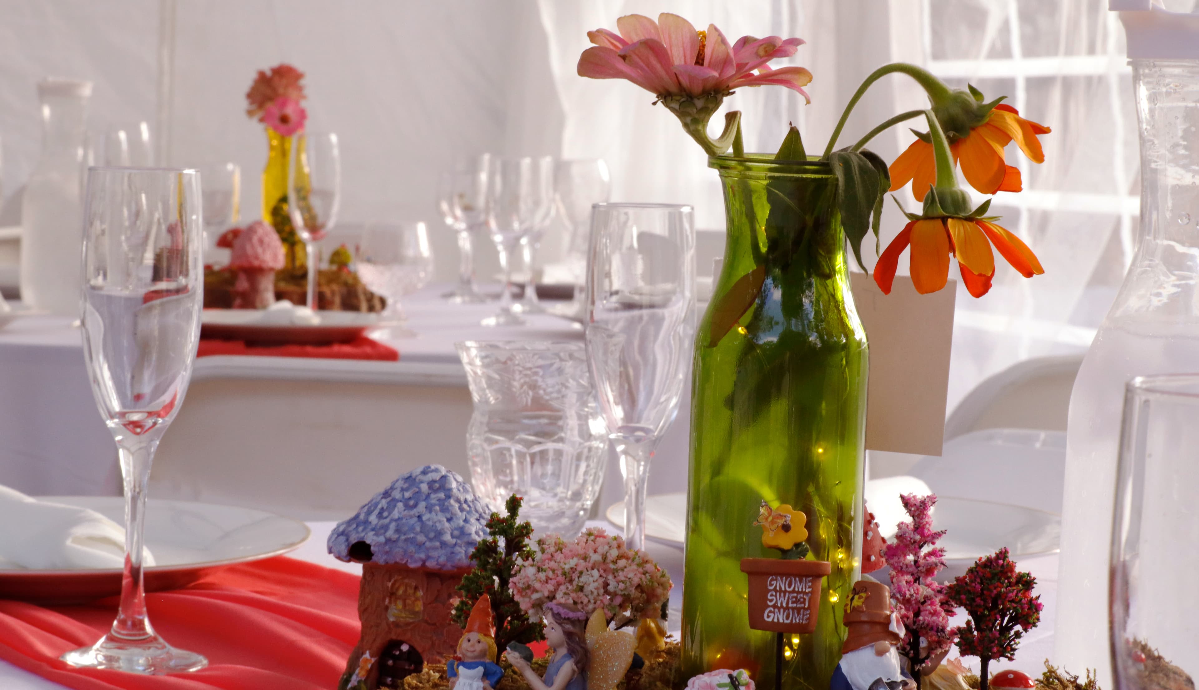 A beautifully decorated table featuring a green vase with vibrant flowers and whimsical gnome figurines.