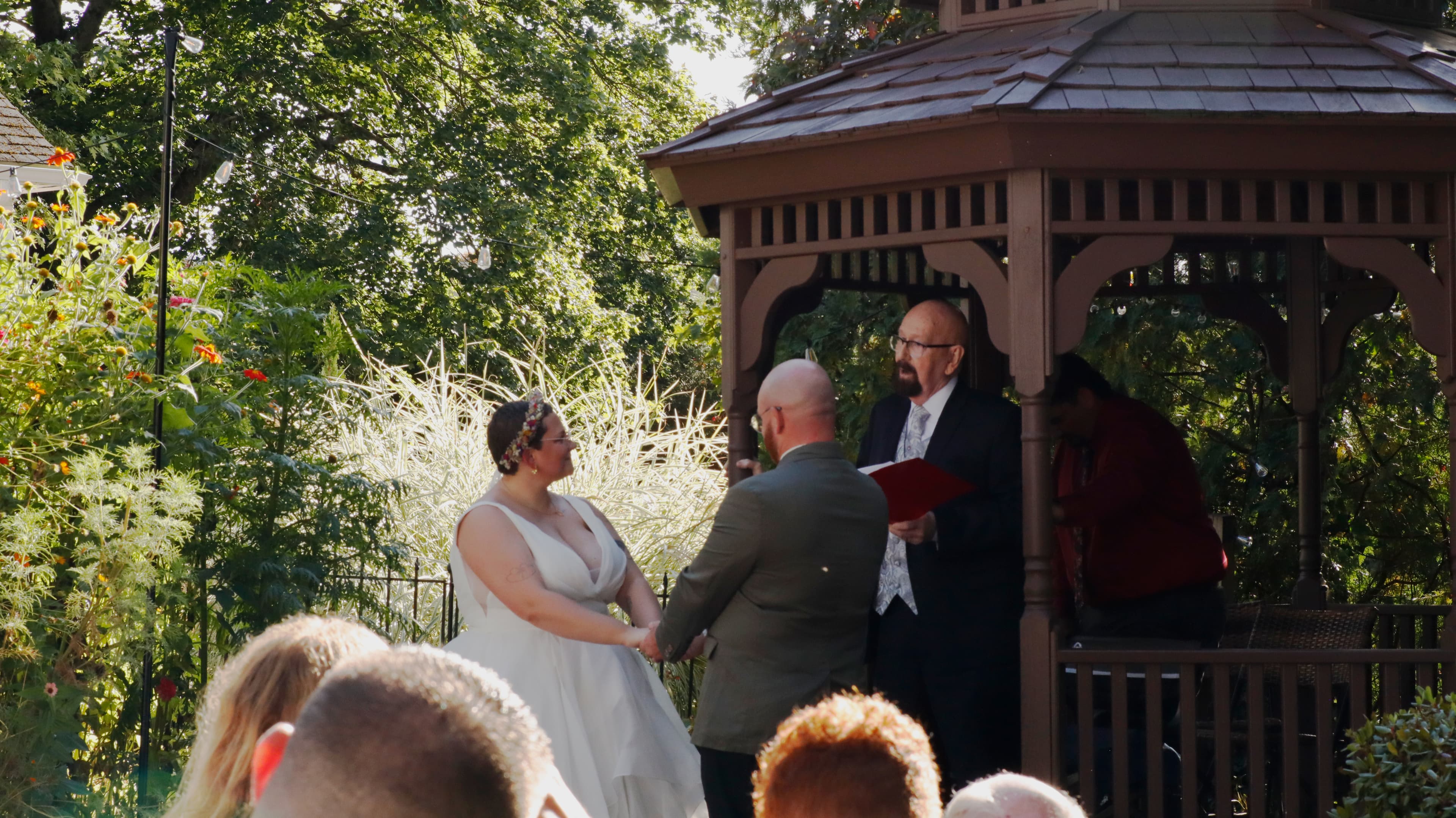 A couple exchanges vows during their wedding ceremony at a gazebo, surrounded by lush greenery.