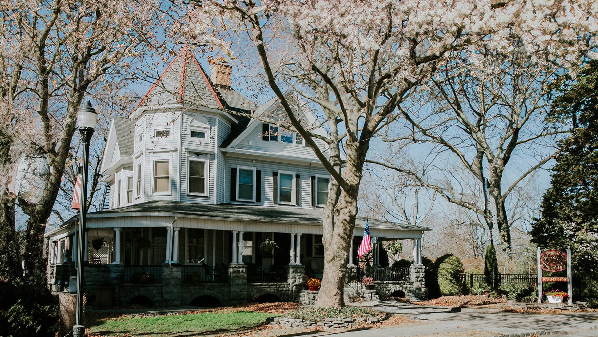 A charming two-story Victorian house surrounded by trees, featuring a wraparound porch and decorative details.