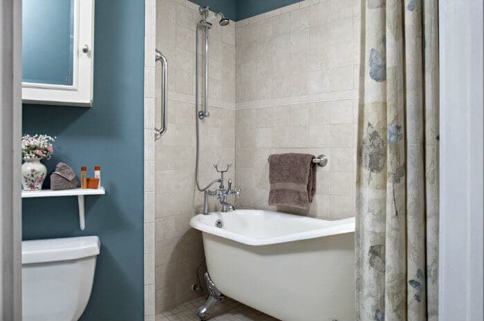 A classic bathroom with blue walls, a clawfoot tub, a toilet, a shower curtain, and a shelf with toiletries.