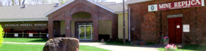 Entrance to Franklin Mineral Museum with Mine Replica display, featuring red brick architecture and large mineral specimen on lawn