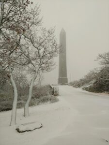 High Point Monument emerging through winter fog, snow-covered path and bare trees in foreground