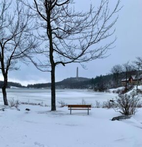 Solitary bench overlooking frozen lake with High Point Monument visible in distance, winter landscape in Sussex County