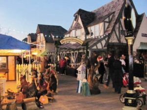 Evening holiday market at Shoppes at Lafayette, Tudor-style buildings decorated for winter with shoppers browsing festive stalls