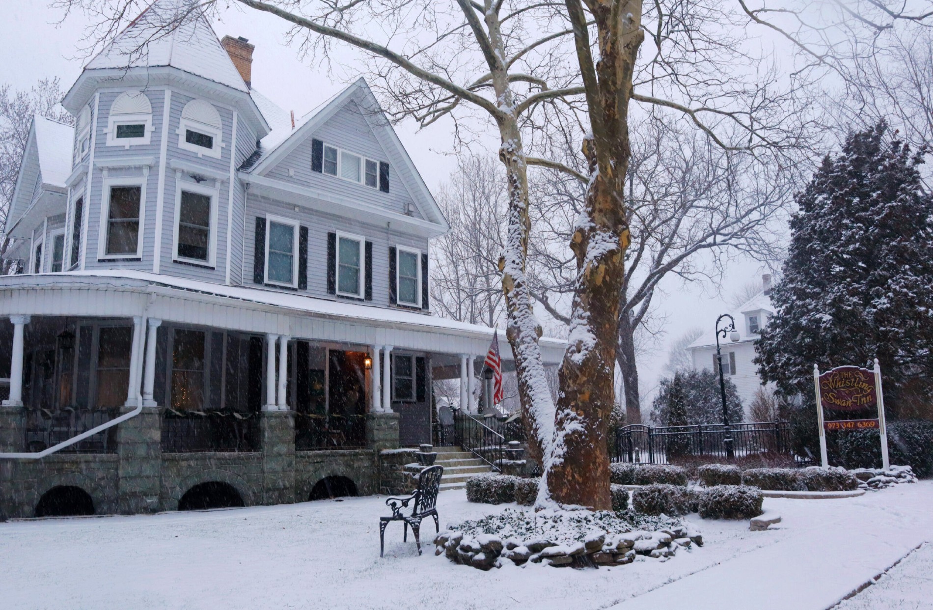 A snow covered lawn, trees and large two story bed and breakfast home