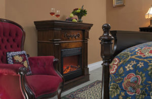 Wooden fireplace next to red wingback chair in tan walled bedroom