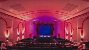 Interior of Newton Theatre with dramatic pink and purple stage lighting, showing historic architecture and modern performance space